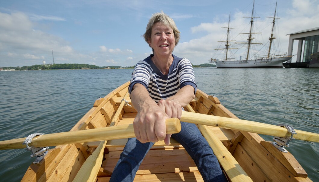 Eva Runesson sitter i båten som hon själv har byggt, ror ut från hamnen i Karlskrona och i bakgrunden syns Marinmuseum och öar i Karlskrona skärgård