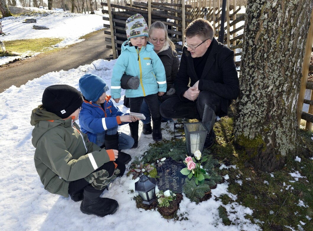 Ewa och Daniel Isaksson med sina söner Wilhelm, 10, Philip, 7, och Johan, 4, på kyrkogården i Hakarp där pojkarnas fyra syskon finns. Gravstenen gjordes till Alice, men här vilar även Mio, Ruth och Esther. Ewa och Daniel Isaksson sitter på huk vid en grav tillsammans med sina tre söner.