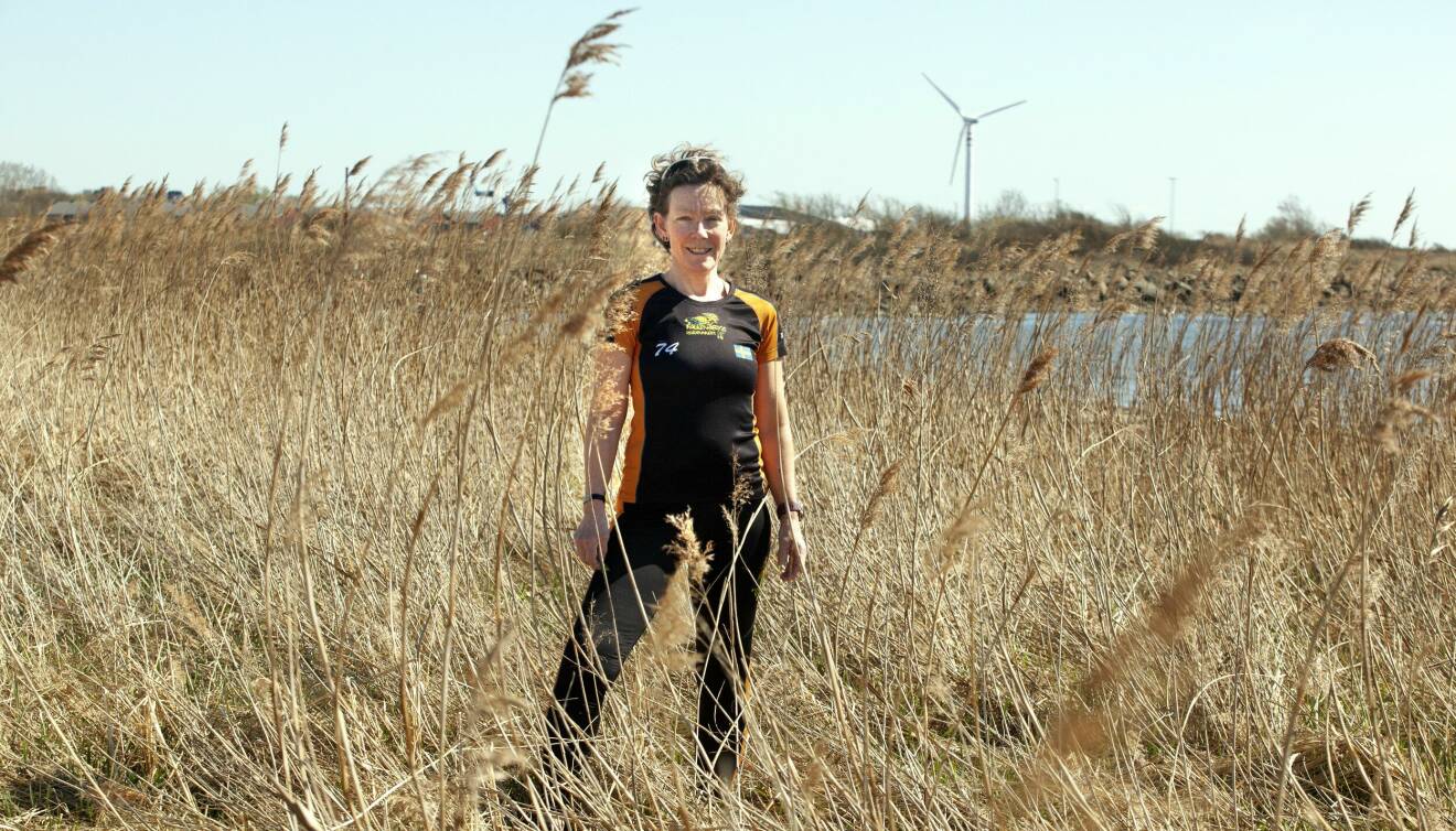 Jessica står i hög vass och i bakgrunden syns vatten och ett vindkraftverk