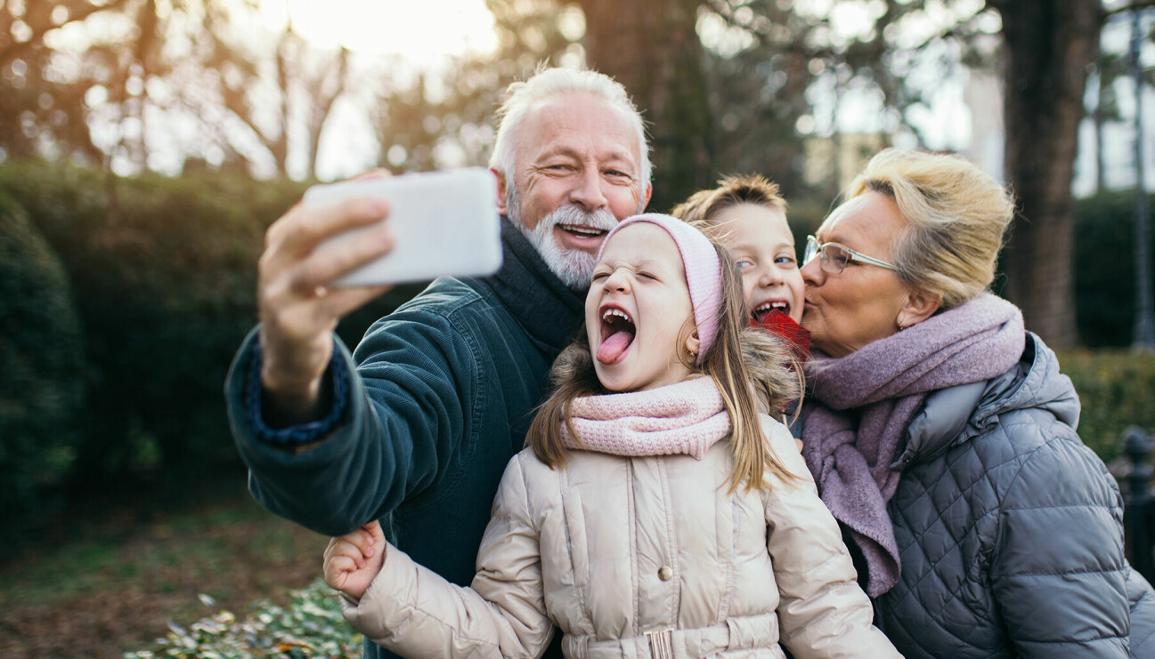 Två farföräldrar tar en selfie utomhus med sina två barnbarn i 8-årsåldern.