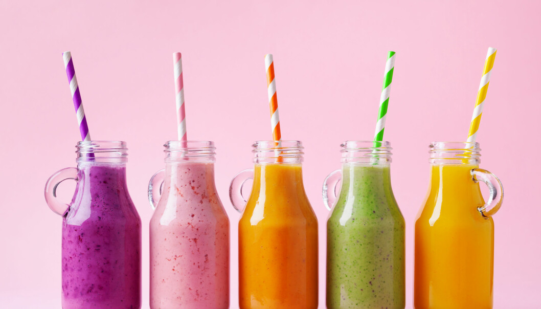 Färgglada smoothies i glasflaskor med randiga sugrör mot en rosa bakgrund.