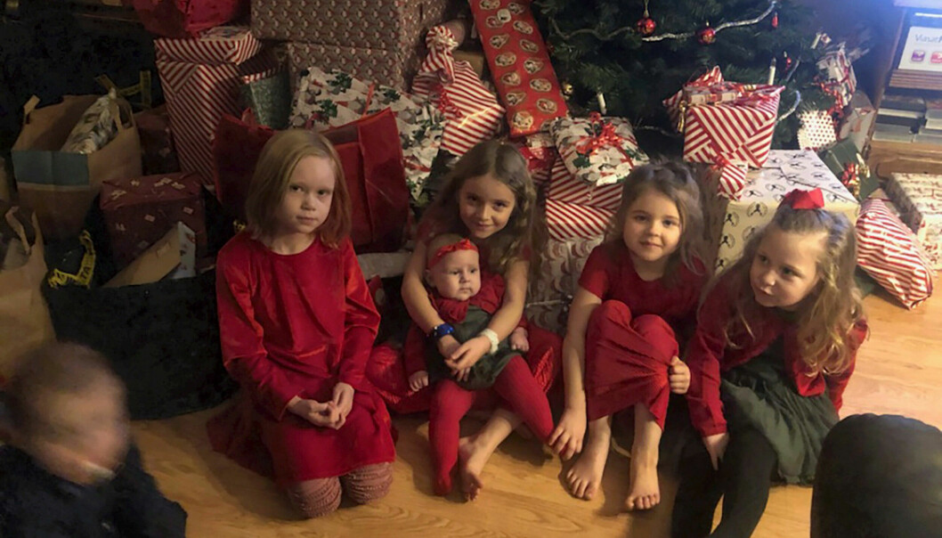 Fem av Irens barnbarn och bonusbarn sitter på golvet framför en stor hög med julklappar som ligger framför en julgran.