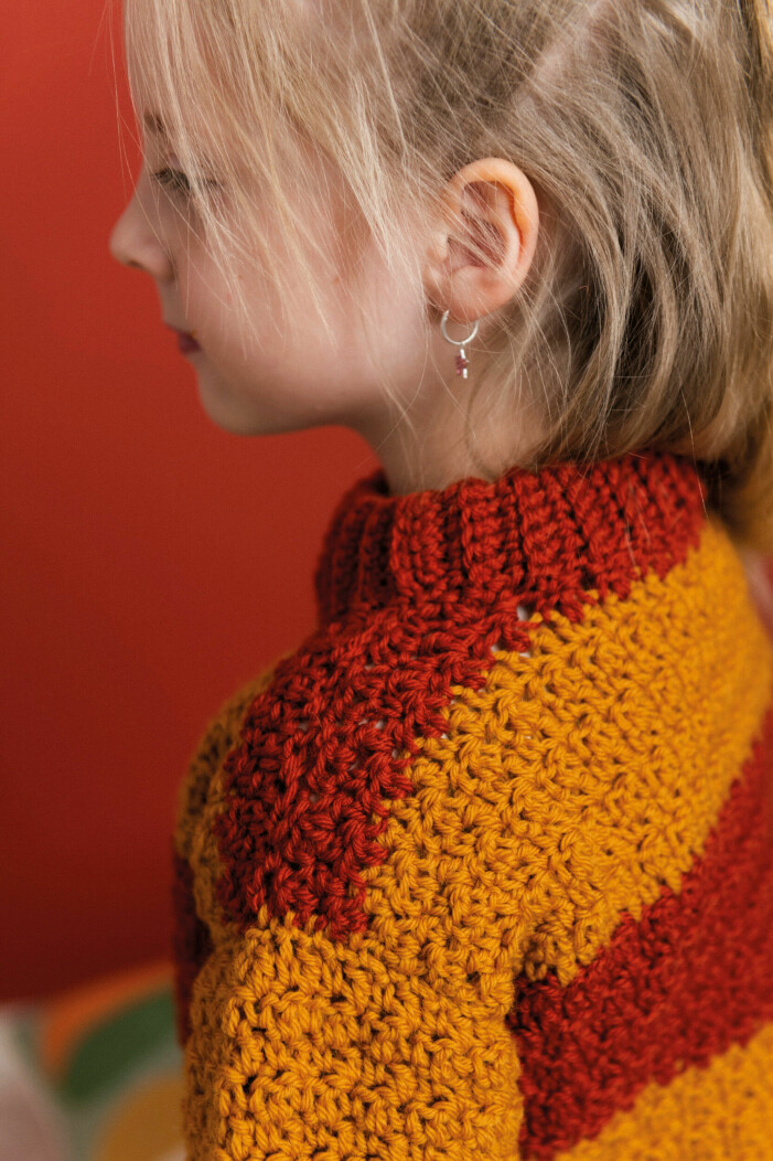 You crochet a front and back piece which are then sewn together. The sleeves are sewn separately and sewn into the armholes. Finally, crochet the neckline. Girl wearing a crochet sweater with stripes.