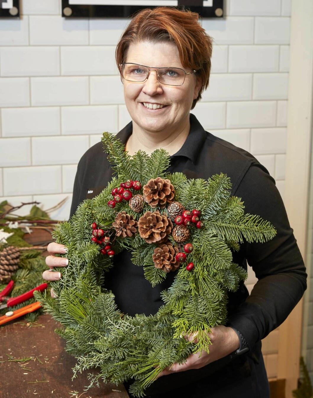Nettan Strahl med den färdiga kransen. Glad florist visar upp krans.