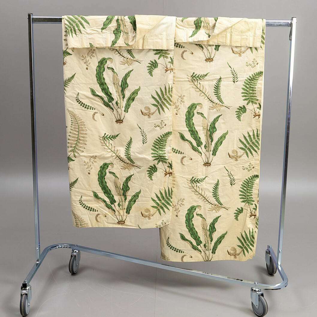 Det fräscha mönstret <span class=" italic" data-lab-italic_desktop="italic">Ferns </span>kallar vi till vardags Stensöta- eller Ormbunkstyget. Motivet kommer från en engelsk flora från 1700-talet och GP & J Baker tog fram det i mitten av 1930-talet. Hos Crafoord Stockholm klubbades ett par bomullsgardiner, 220x124cm vardera, för 1800kr tidigare i år. Två bitar av mönstret Ferns hänger på en klädställning.