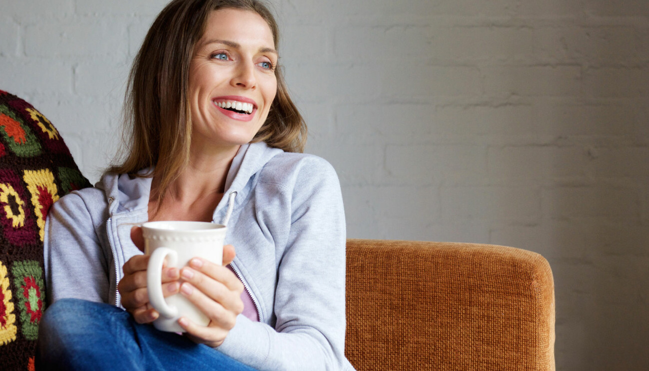 Glad kvinna dricker te i soffan.