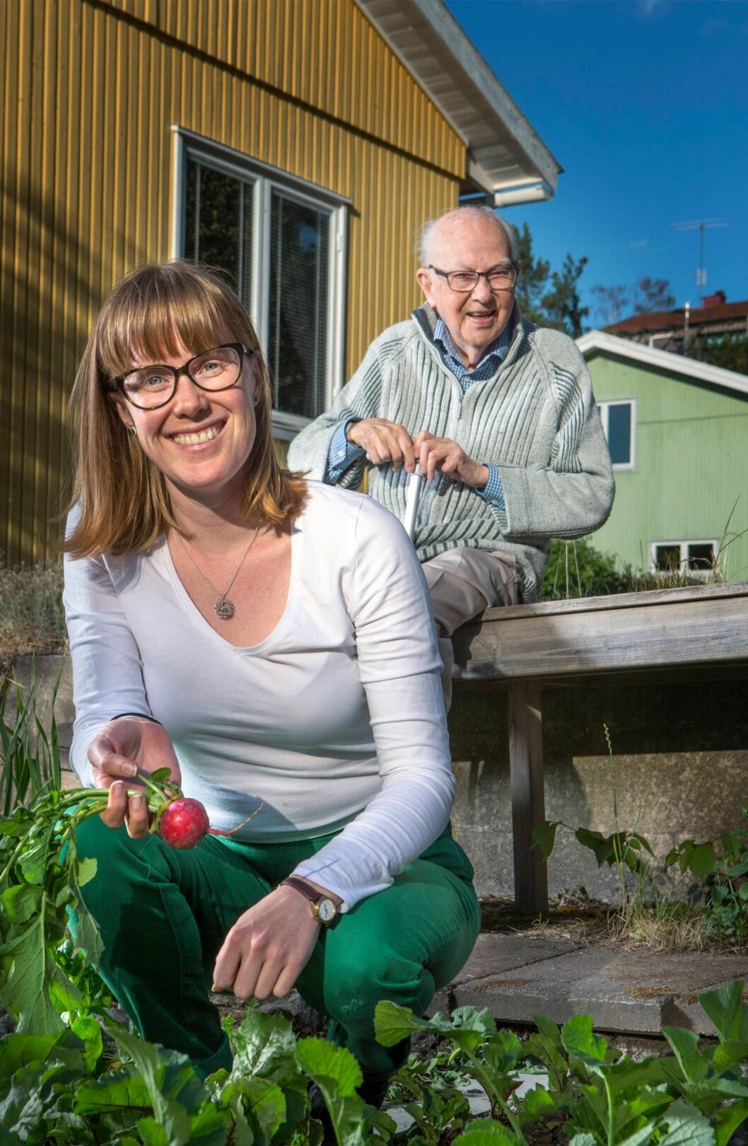 En ung kvinna med en rädisa i handen sitter på huk framför en äldre man.