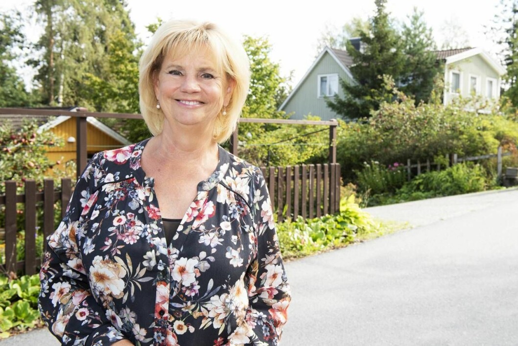 Marianne på Höganloftsvägen. På bilden skymtar barndomshemmet, det gröna huset, i bakgrunden. Foto: Theresia Köhlin. Marianne framför sin barndoms hus.