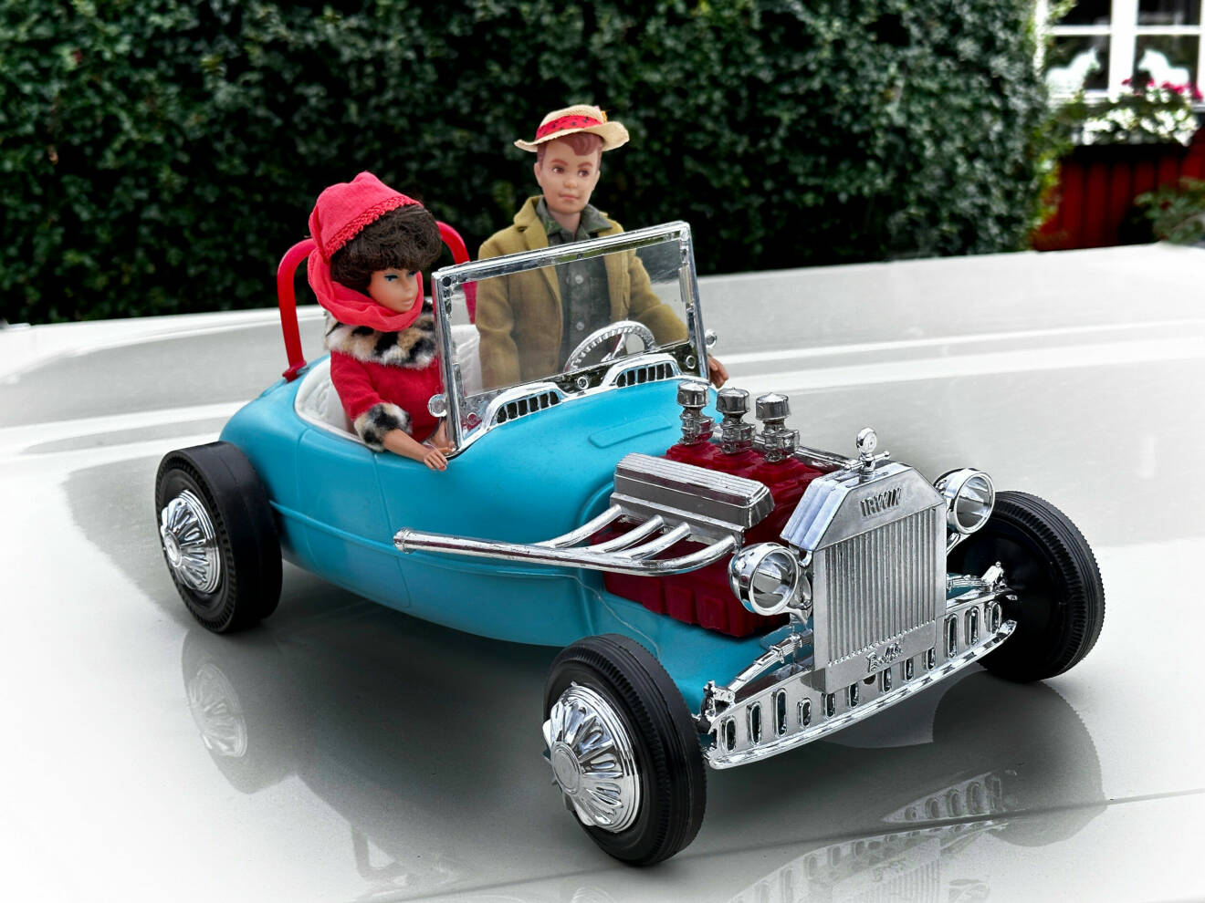 En barbie och en Ken sitter i en blå vintage roadsterbil.