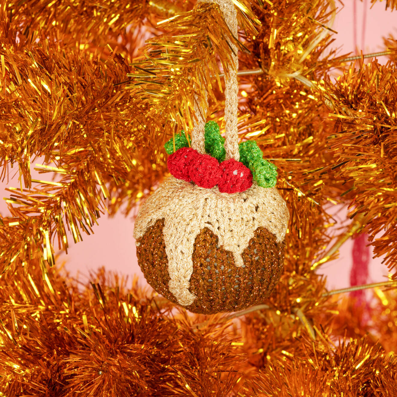 En stickad julgranskula hänger i en kopparfärgad gran.