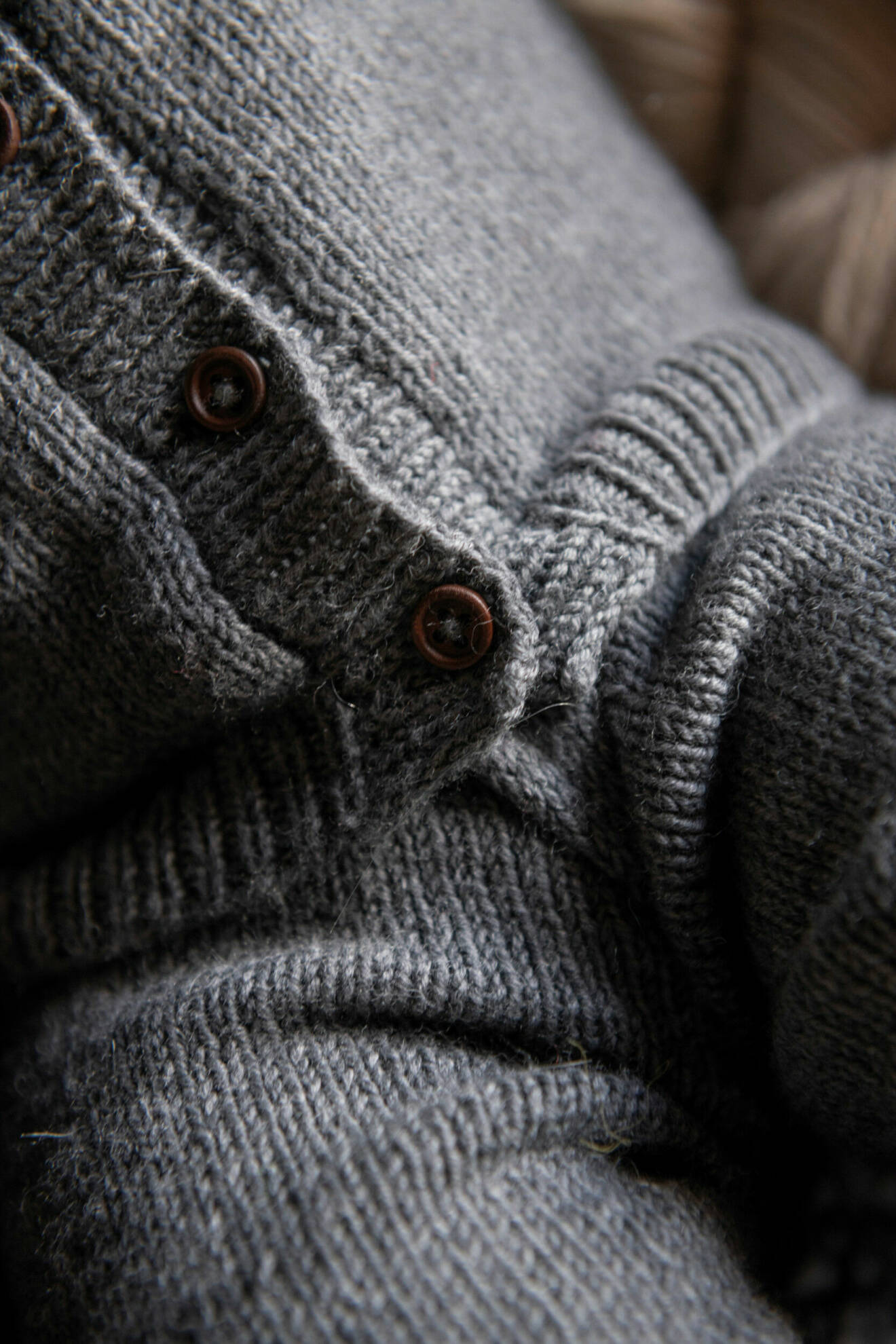 Detaljbild på stickad grå babykofta med resår och bruna knappar.