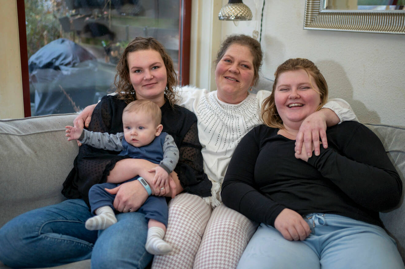 Carina Bigands sitter i soffan och kramar om sina två döttrar. Med är även hennes barnbarn.