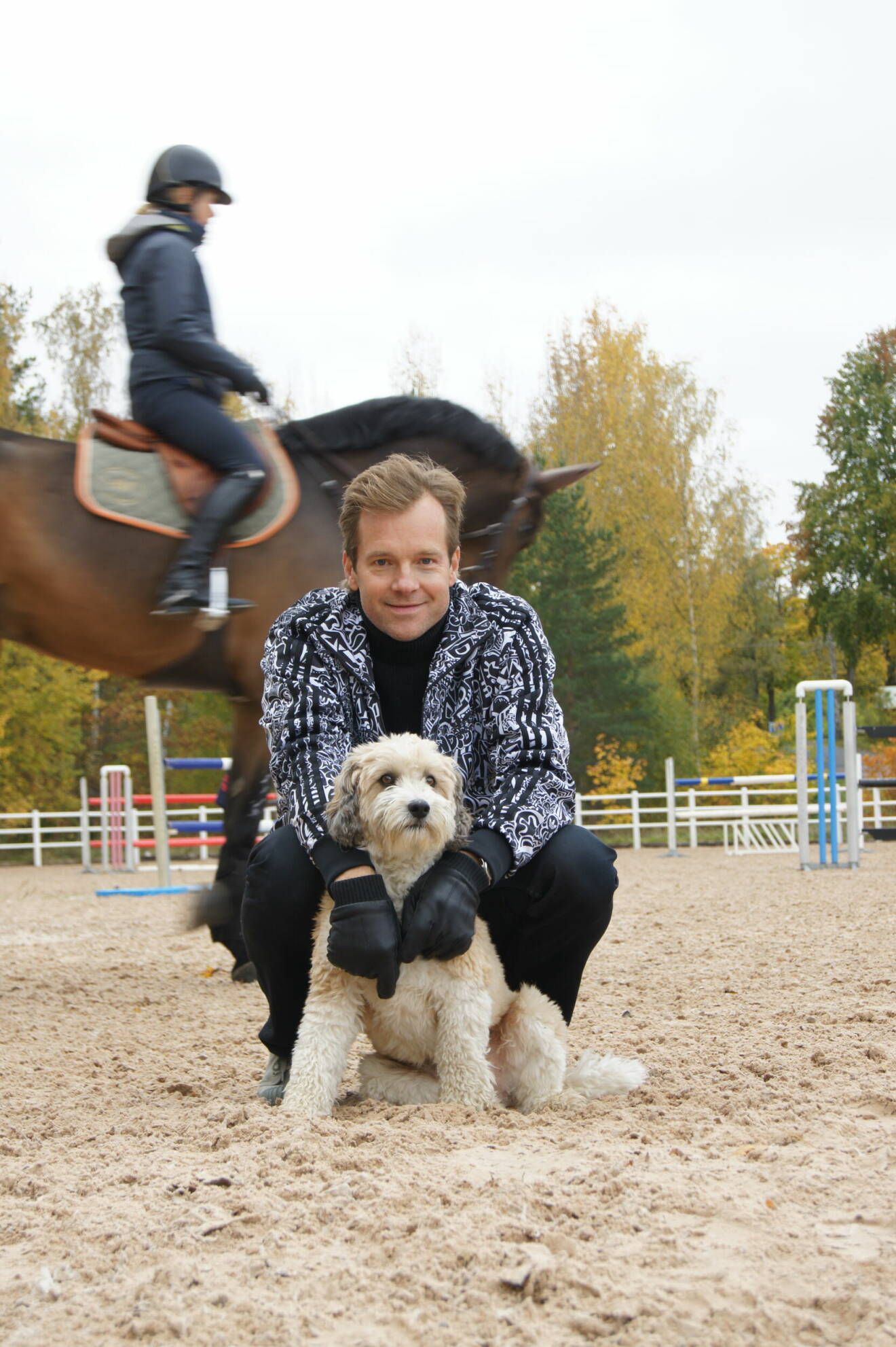 Henrik Johnsson på huk tillsammans med en hund, medan en häst passerar bakom honom.