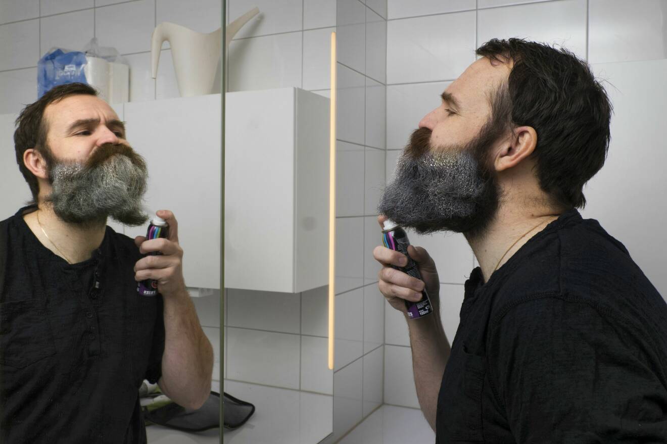 Tobias speglar sig och sprayar grå spray i sitt skägg.
