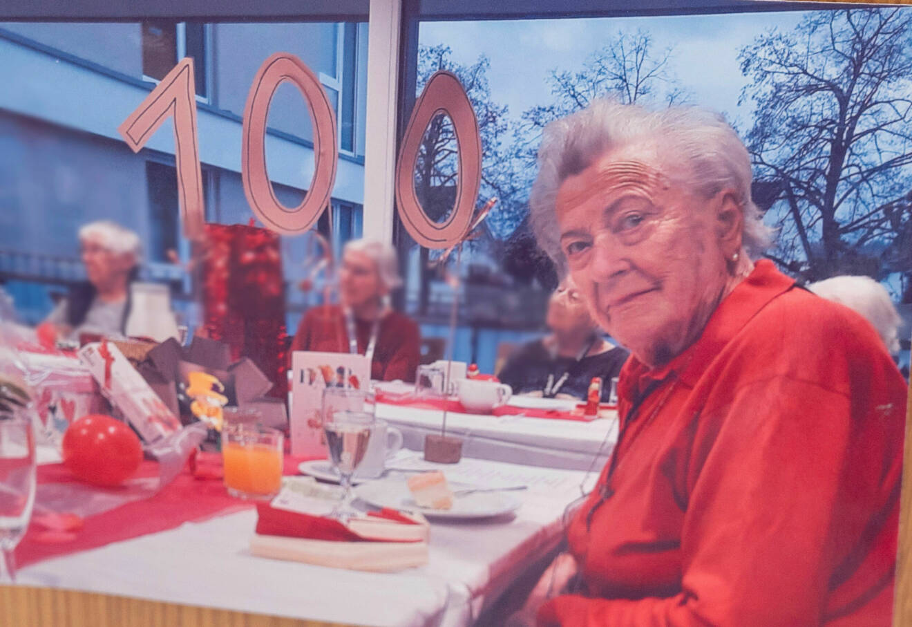 Äldre dam sitter vid ett dukat bord på ett 100-årsfirande.