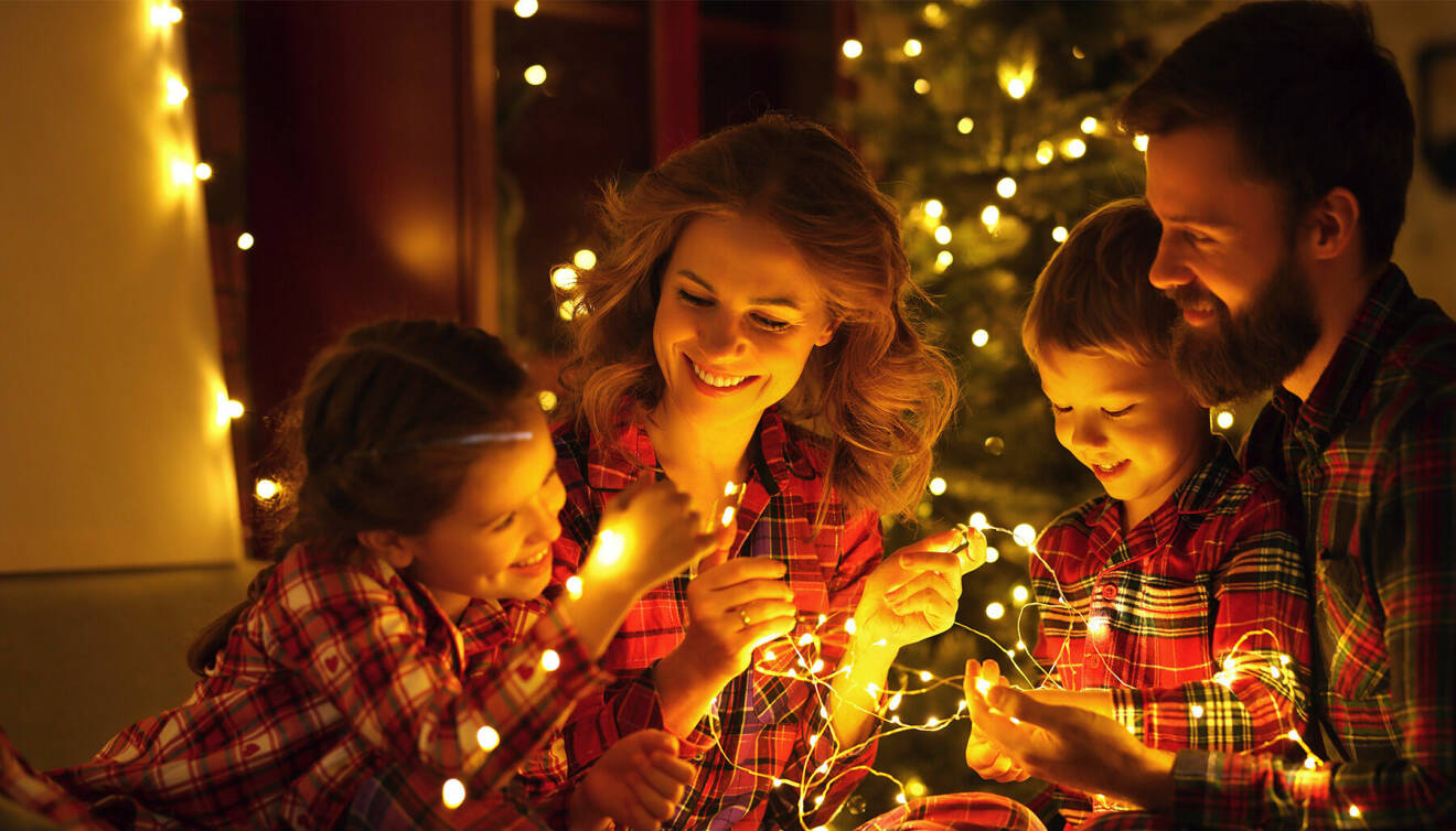 Familj sitter tillsammans i julpyjamas på golvet och håller i en ljusslinga.
