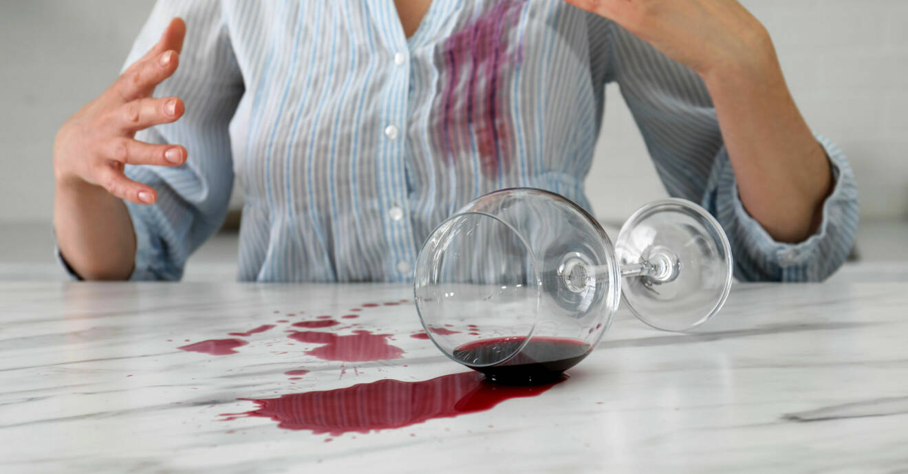 En kvinna har spillt ett glas rödvin på bordet och på sin skjorta.