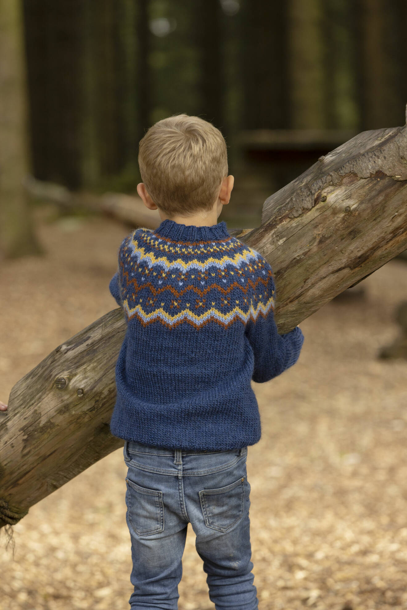 En pojke står med ryggen mot kameran och har på sig en stickad tröja.