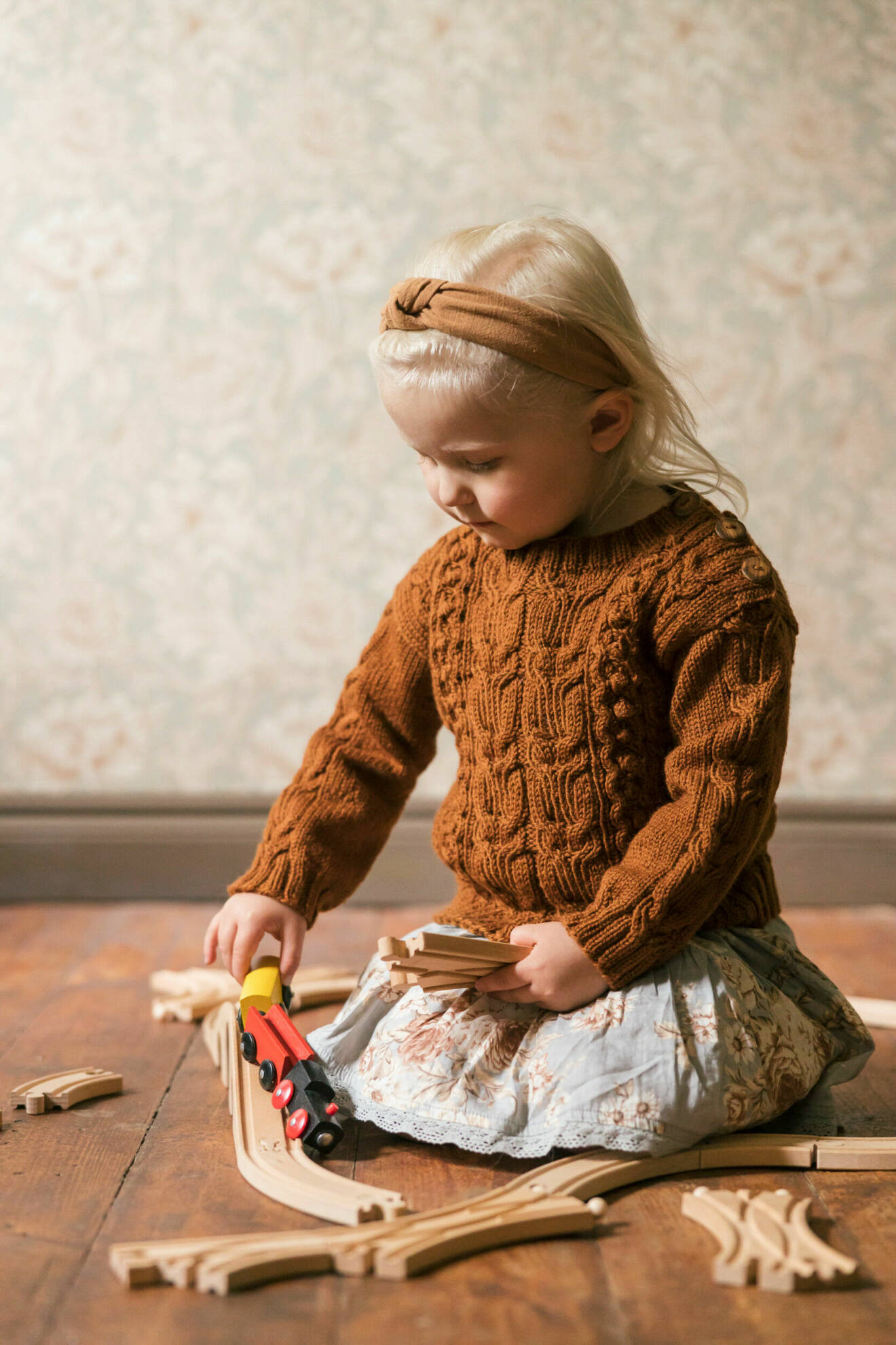 Flicka har på sig en stickad tröja och leker med ett leksakståg.