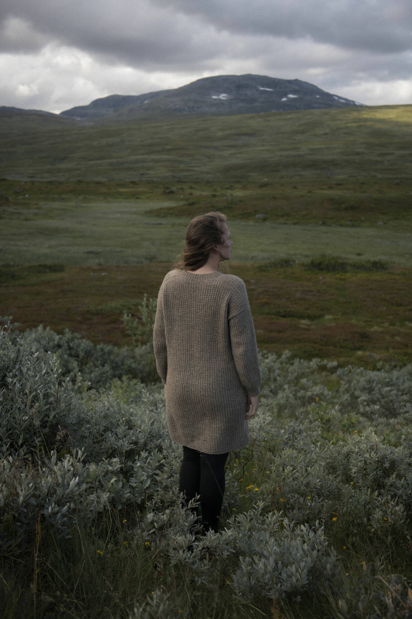 Kvinna står på ett grönt fält med ryggen mot kameran.