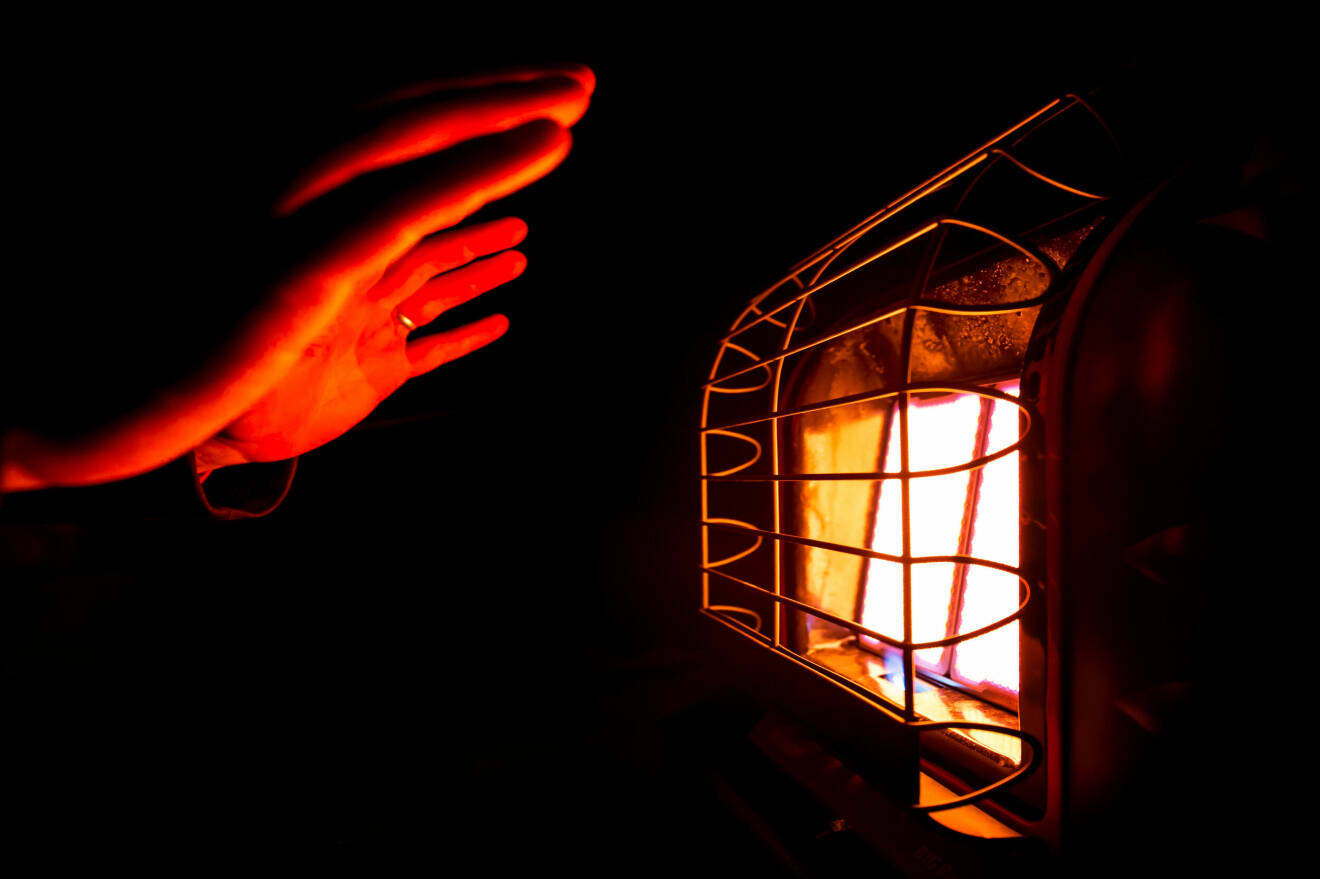 En person värmer sina händer mot en gasolvämare.