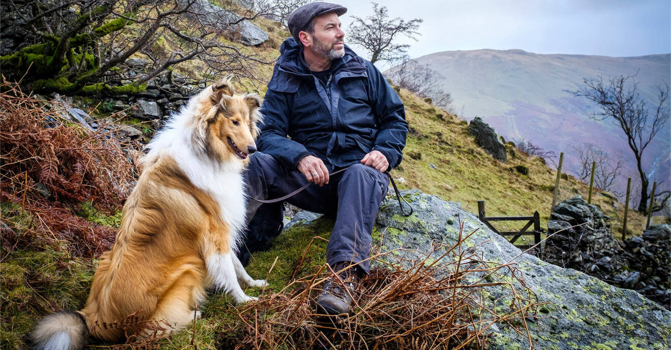 En man sitter i naturen tillsammans med sin hund.