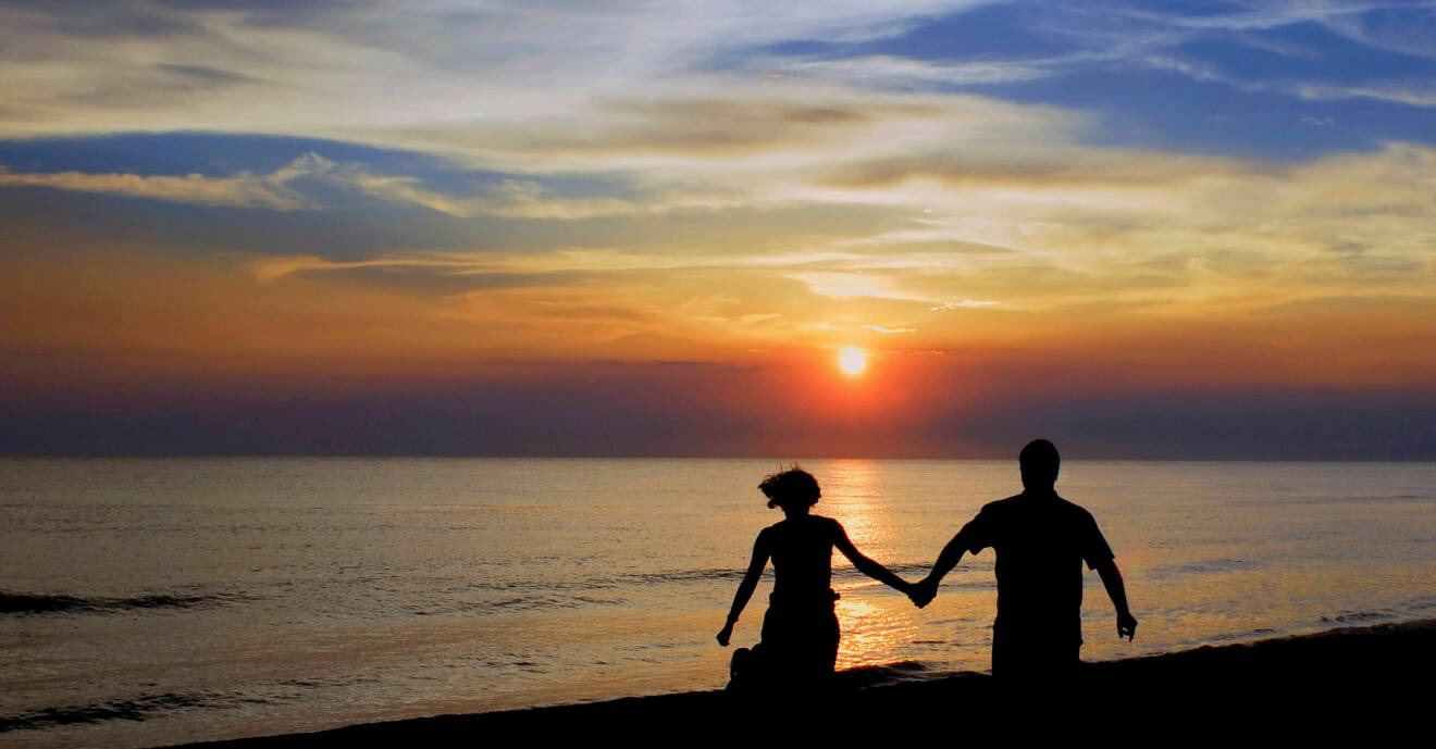 Ett par går hand i hand i solnedgången på en strand.