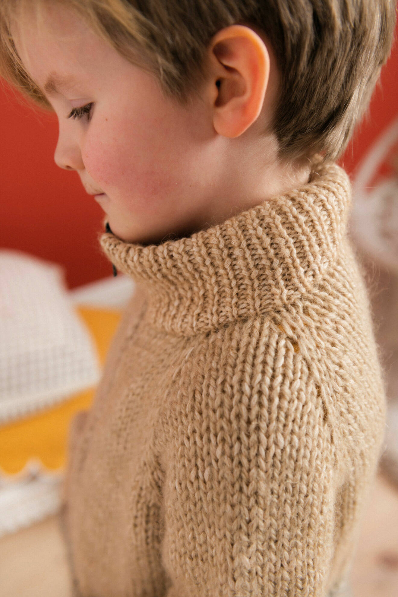 Närbild på en pojke iklädd en beige stickad tröja stående i profil.