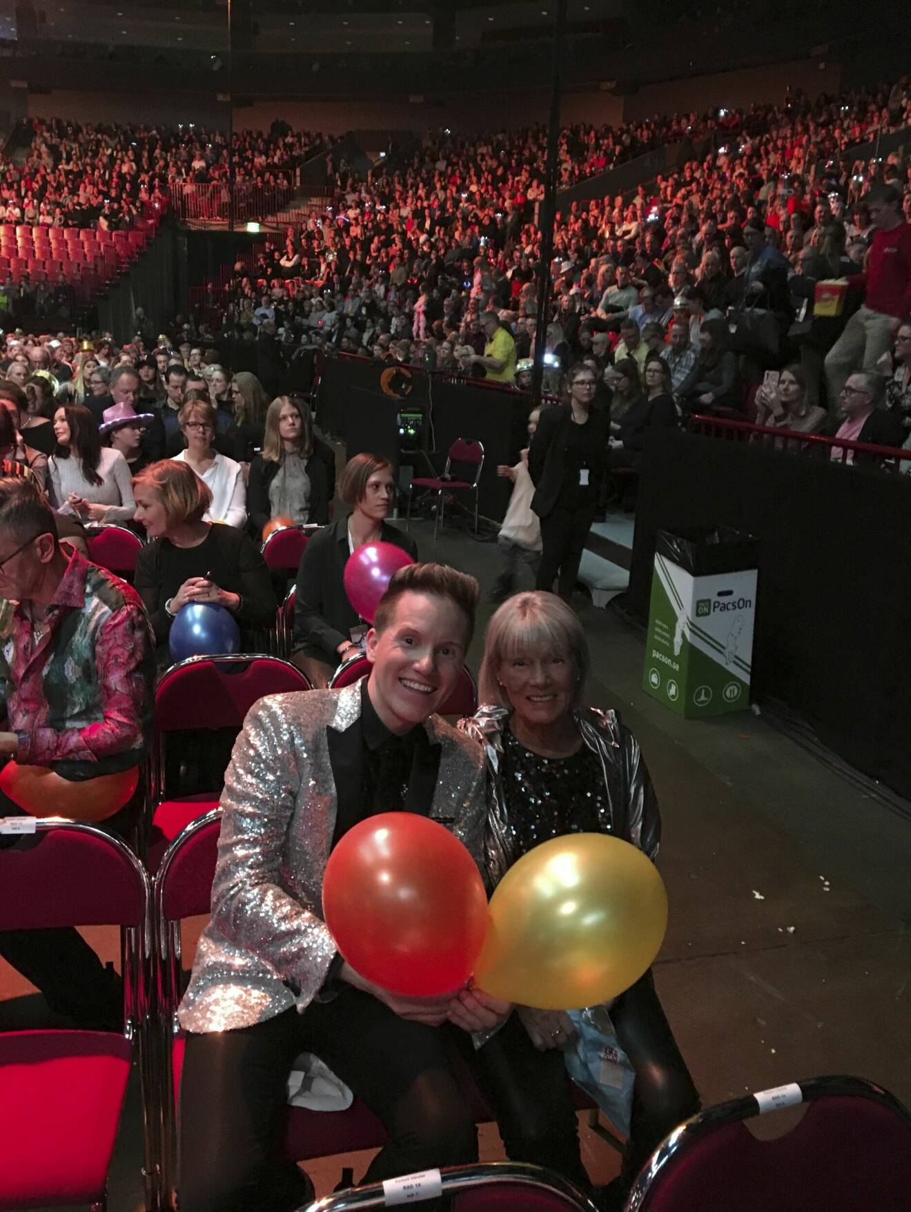 Johan Svensson med sin mamma Christel i publiken under Melodifestivalen. De håller i två ballonger.