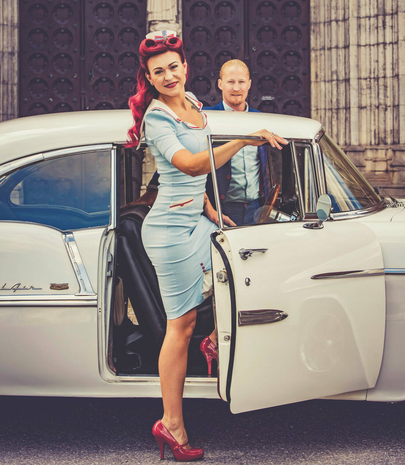 Nygifta Ida i ljusblå klänning kliver in i en vit 50-talsbil, och på andra sidan bilen står maken Henrik i blå kostym.