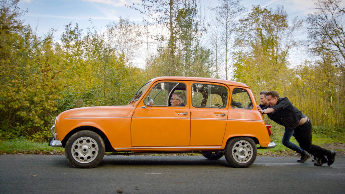 Filip och Fredrik puttar en gammal orange bil osm Lars Hammar sitter i.