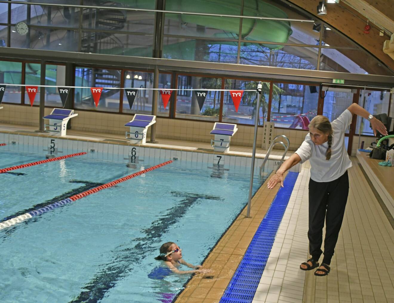 Kicki Eriksson, som står på bassängkanten, visar sexåriga Ellen Persson i poolen hur hon ska röra armarna när hon crawlar.