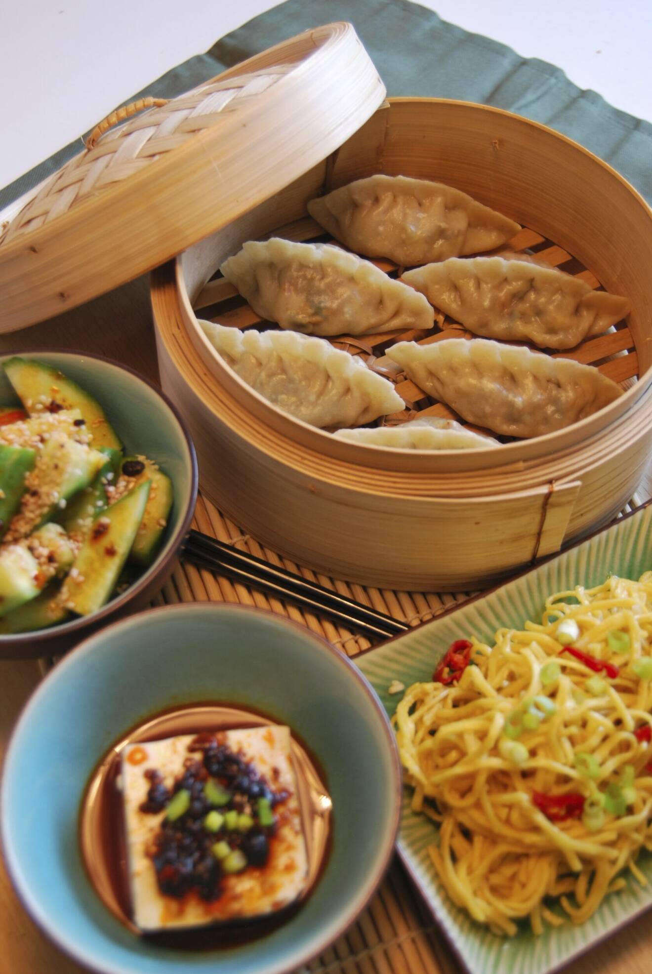 En bild på olika typer av asiatisk mat bland annat dumplings, gurksallad och nudlar.