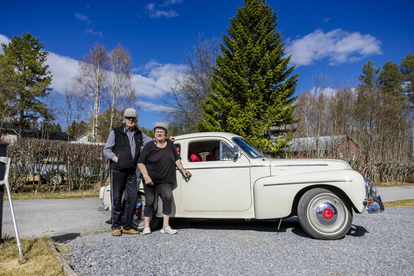 Gunnar och Sonja Flodström står vid sin vita Volvo PV och bär bilhjälmar på huvudena.