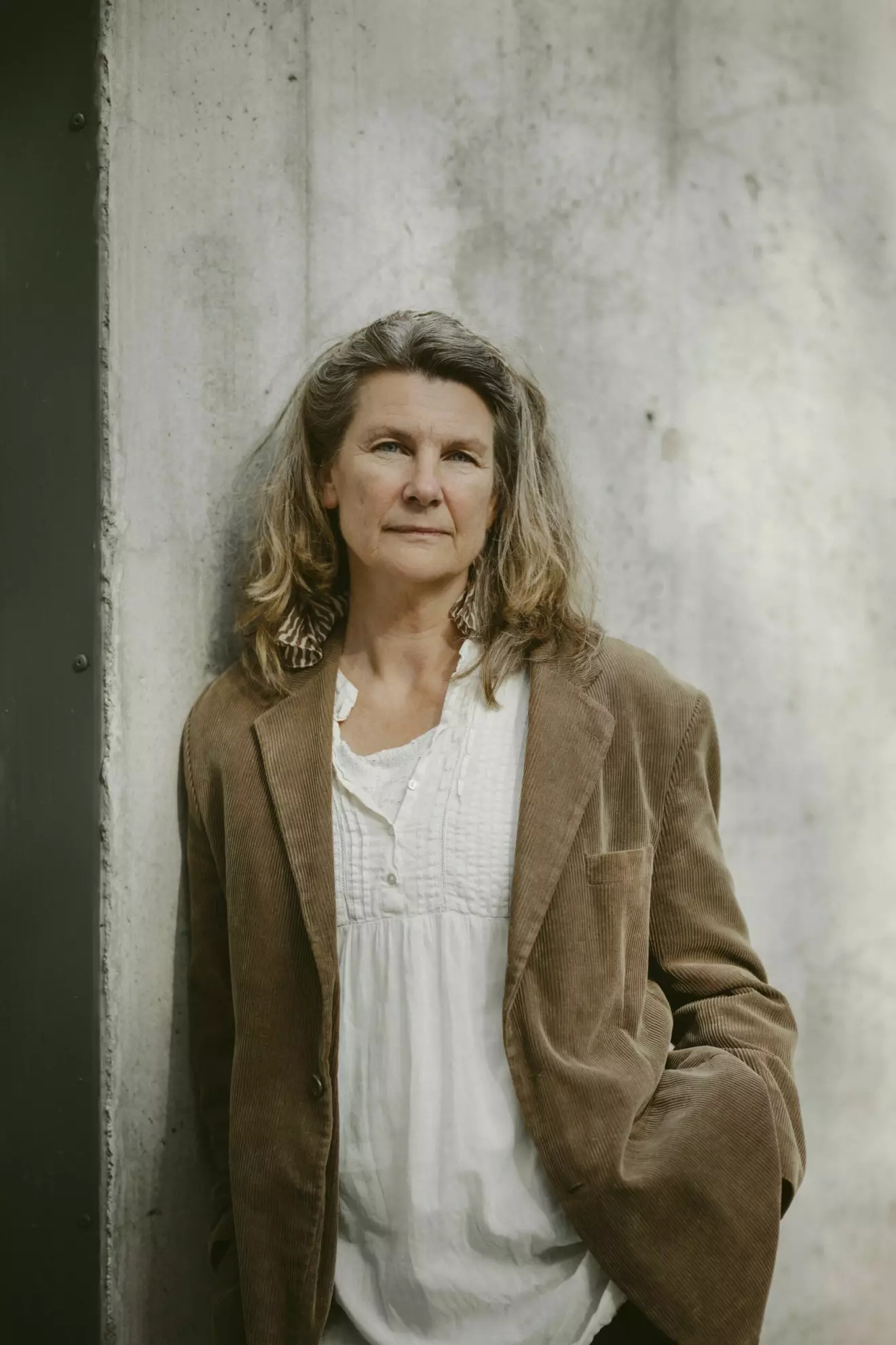 SVT-reportern Lena Pettersson står lutad mot en grå betongvägg. Hon har på sig en brun manchesterkavaj och en vit blus.