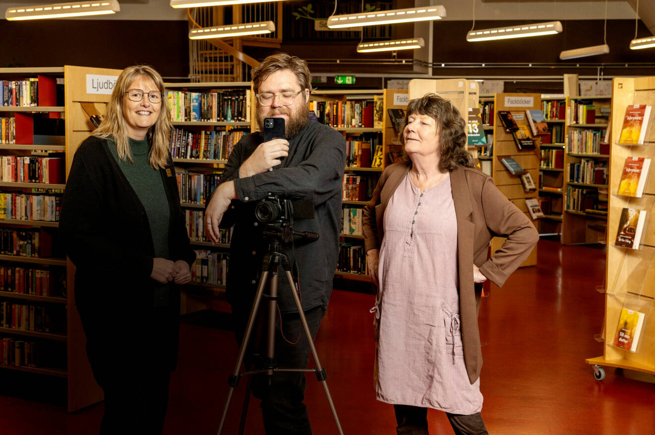 Kollegor på bibliotek står vid bokhyllor med kamerautrustning