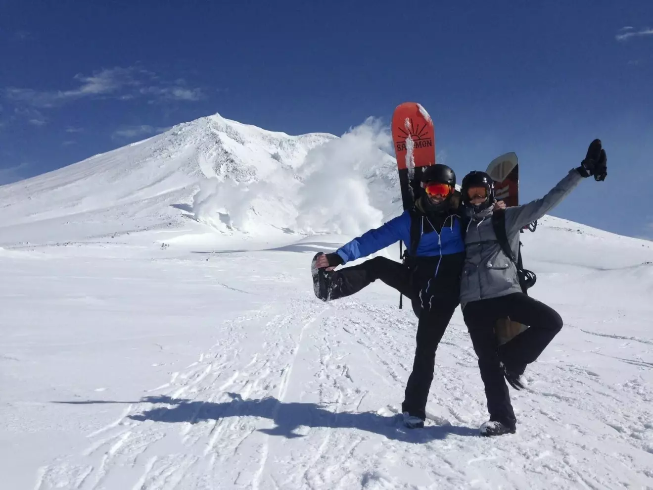 Ett par ler mot kameran i en skidbacke. De har snowboards på ryggen.