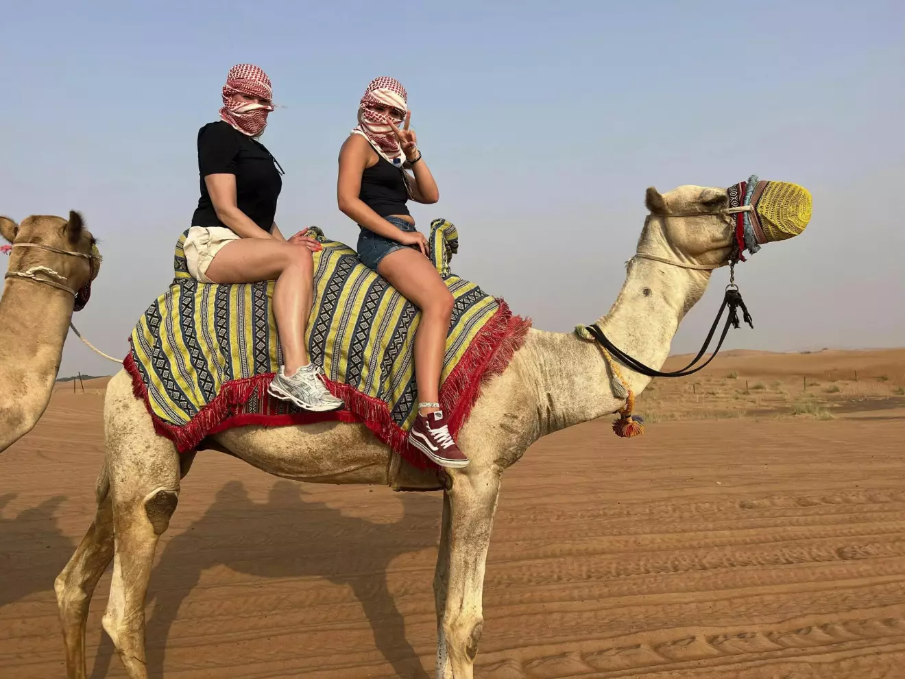 Två kvinnor sitter på en kamel. En av dem gör peace-tecken.