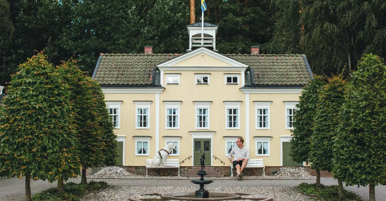 Hund och husse på varsin dockstor soffa framför ett hus på Astrid Lindgrens värld.
