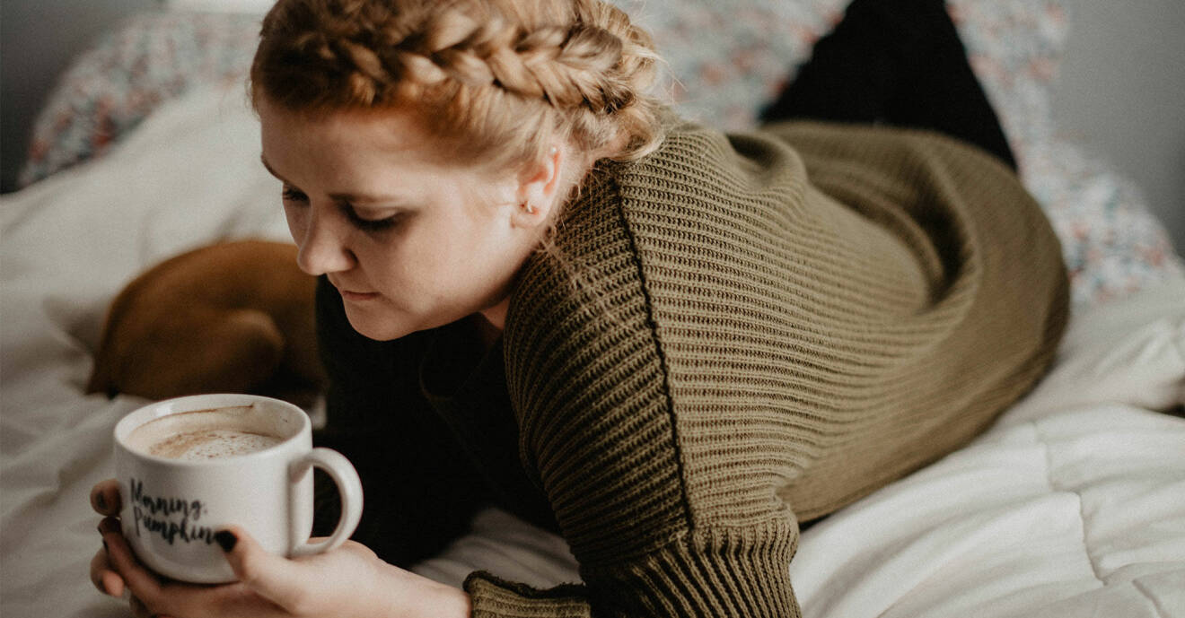 Kvinna som ligger ensam på en säng med en kopp kaffe.