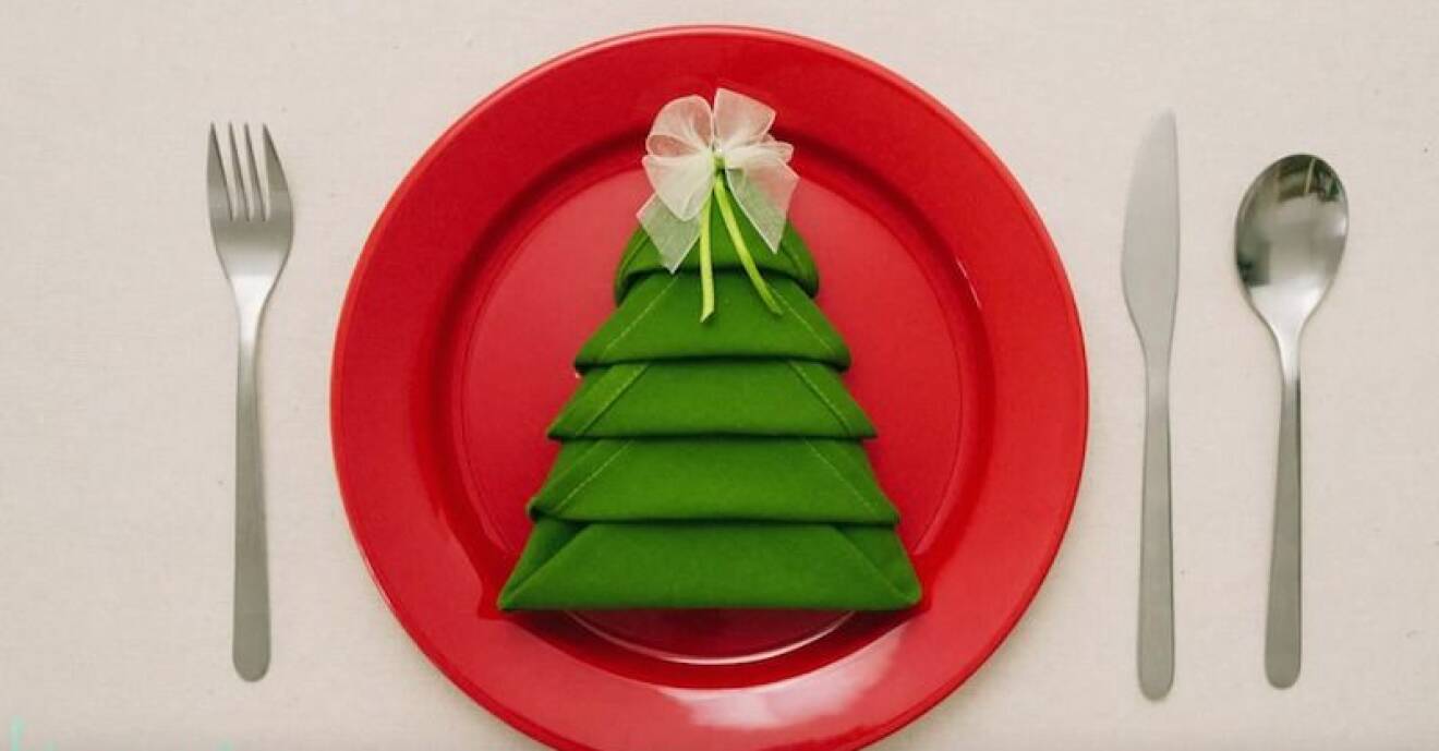 En röd tallrik med en grön servett vikt som en julgran.