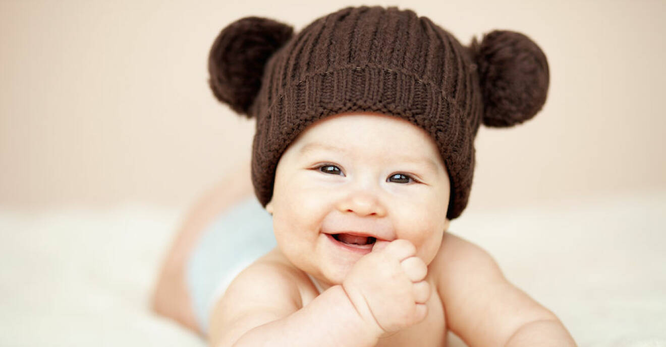 En bebis med en teddymössa skrattar in i kameran.