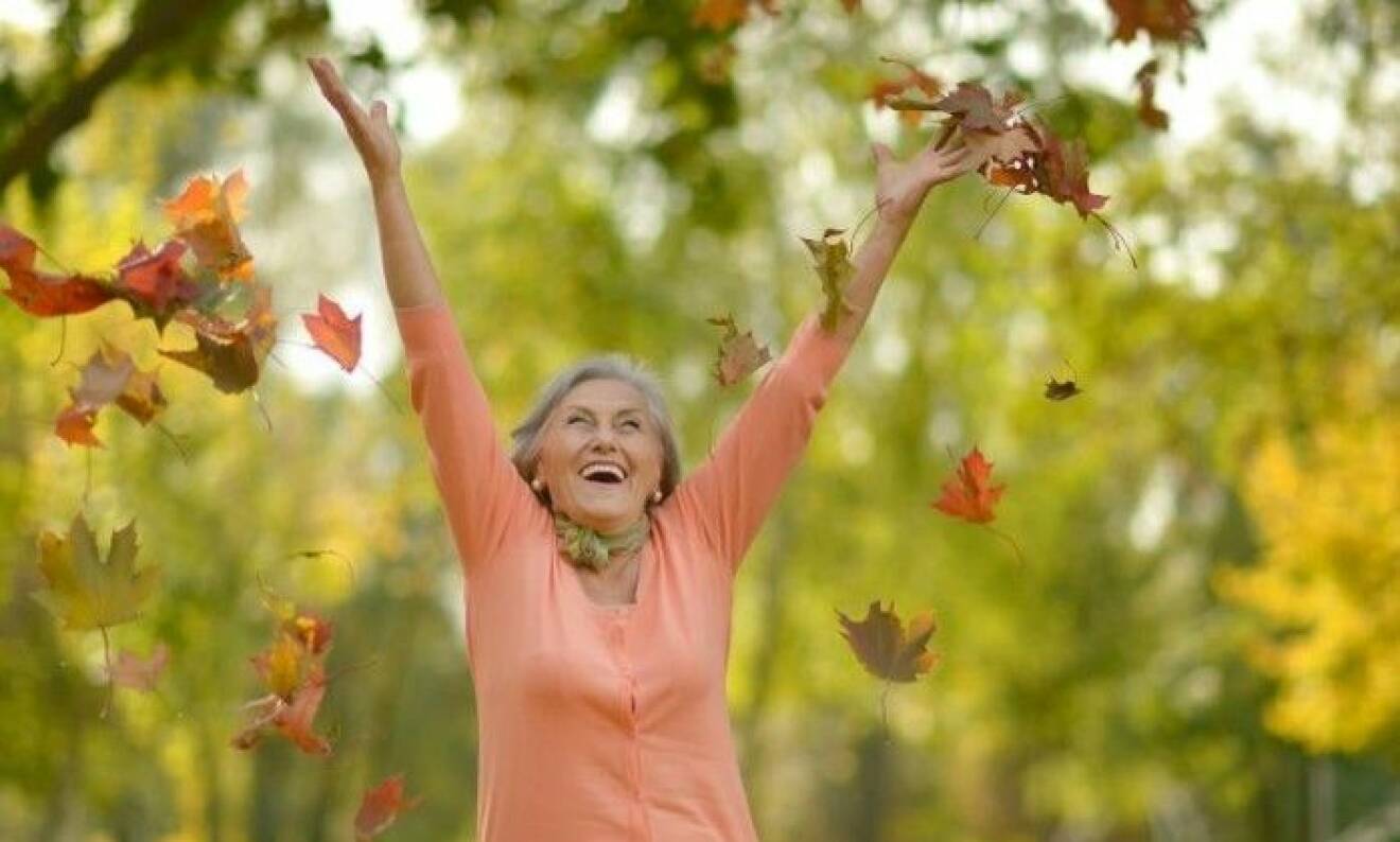 Äldre lycklig kvinna som kastar höstlöv