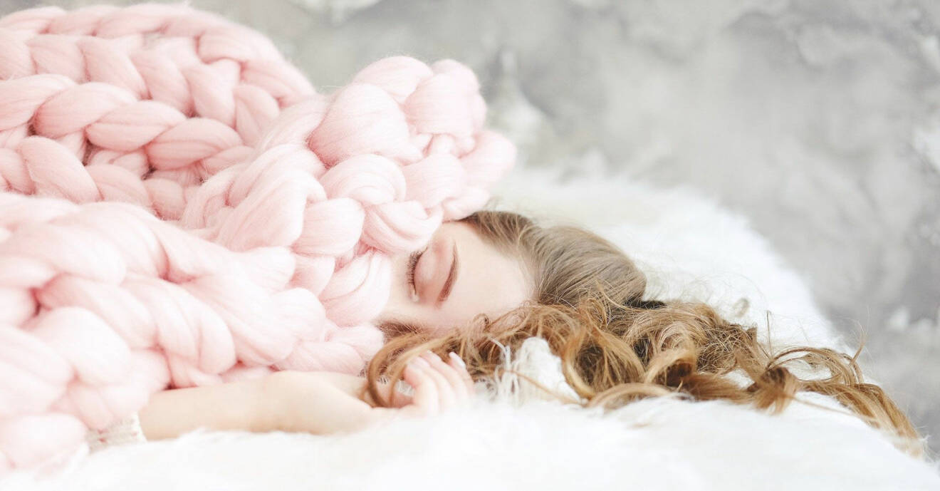 Kvinna med brunt hår sover i sängen täckt av en filt.