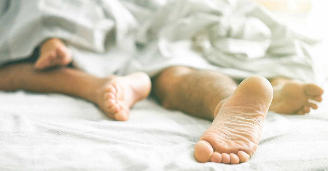 Ett par ligger tätt omslingrade i en säng. VI ser bara fötterna.
