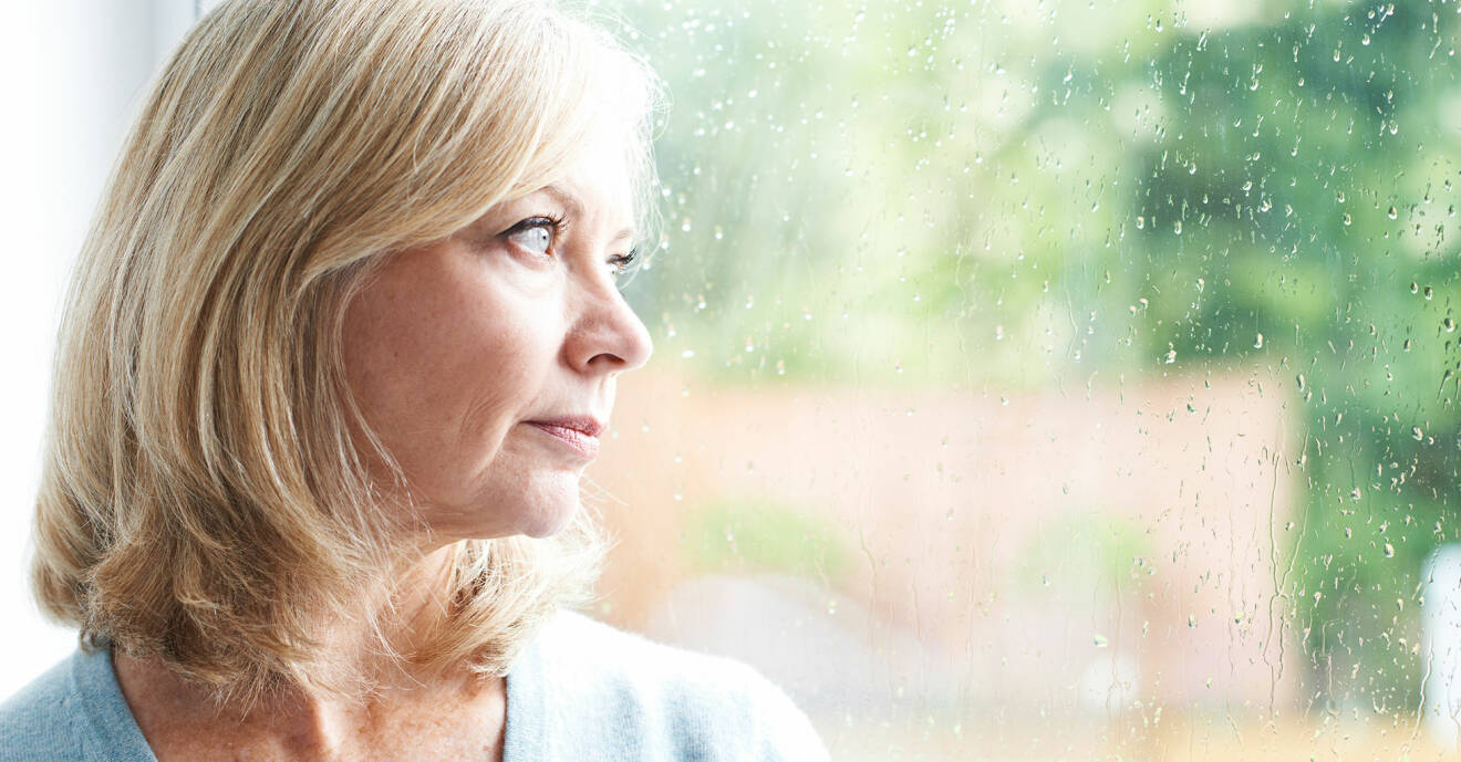 Kvinna tittar ut på regnet genom ett fönster