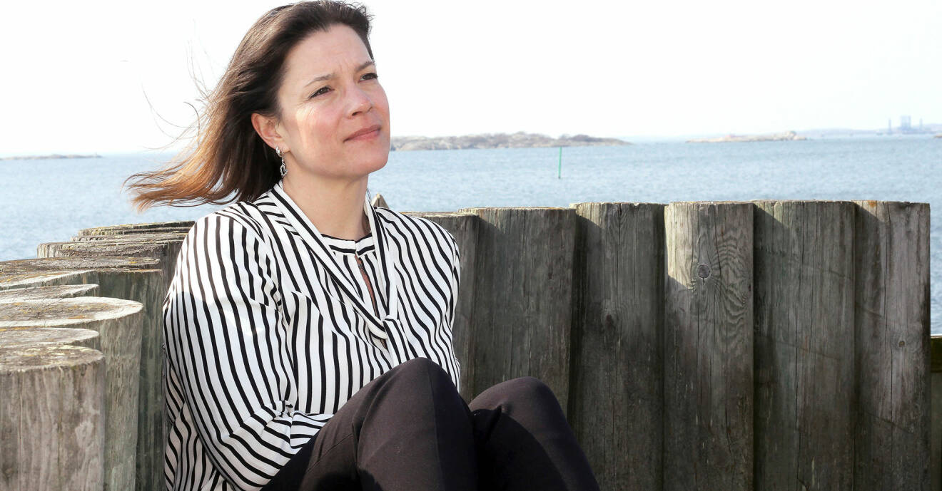 Anne-Liv sitter mot en trämur med havet i bakgrunden