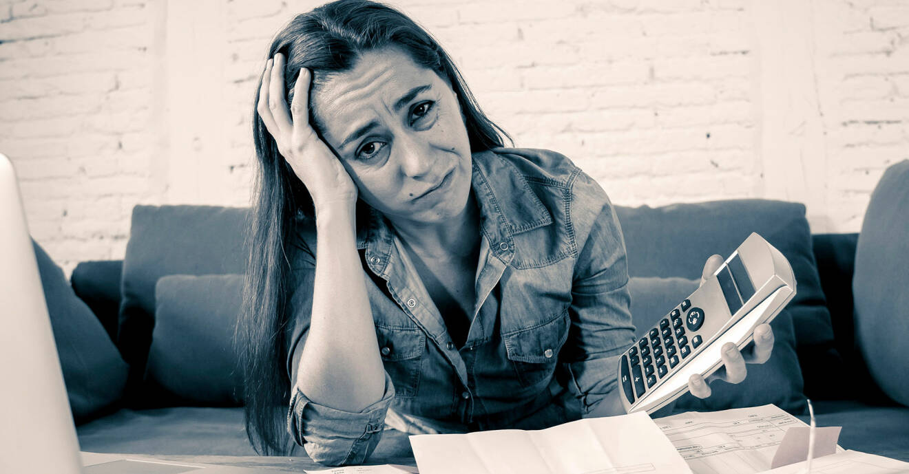 Kvinna sitter med en dator och miniräknare och ser stressad och ledsen ut