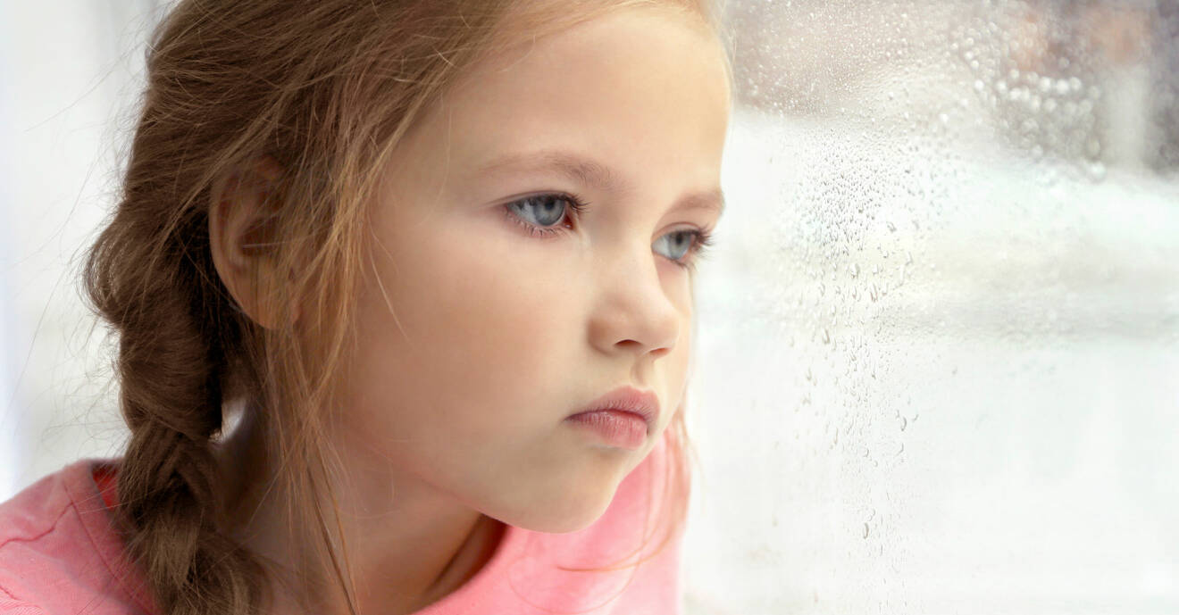 Liten flicka ser ledsen ut och tittar ut genom fönstret