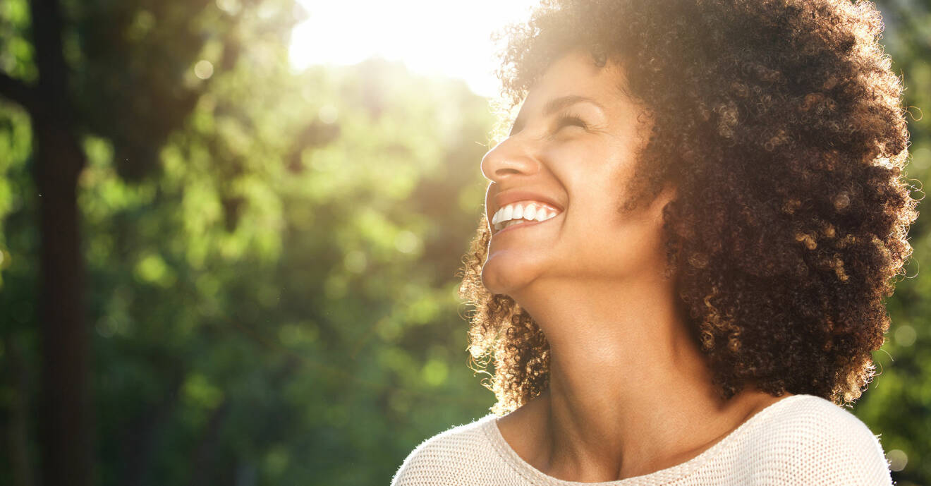 Kvinna ler mot solen med grönskande bakgrund